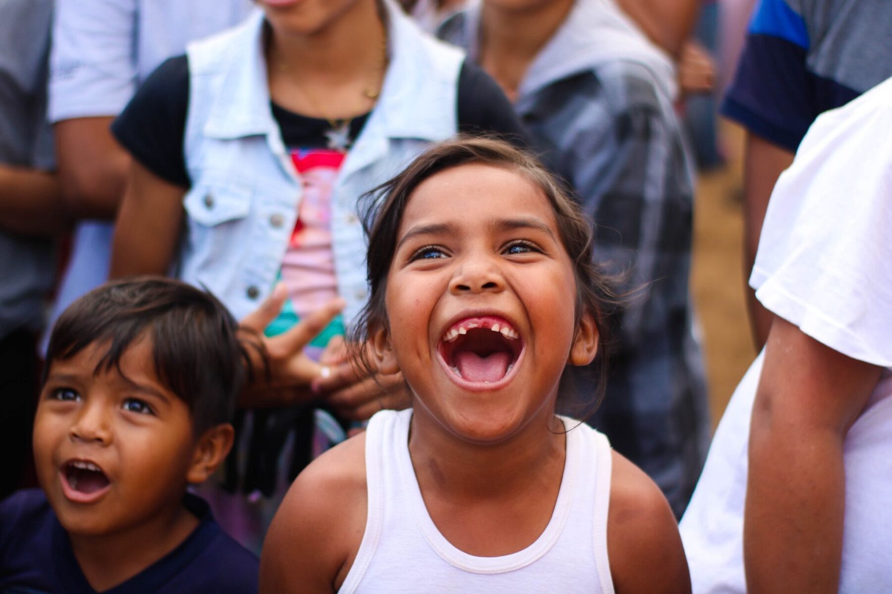 Two young children laughing with open-mouthed joy at an outdoor community event