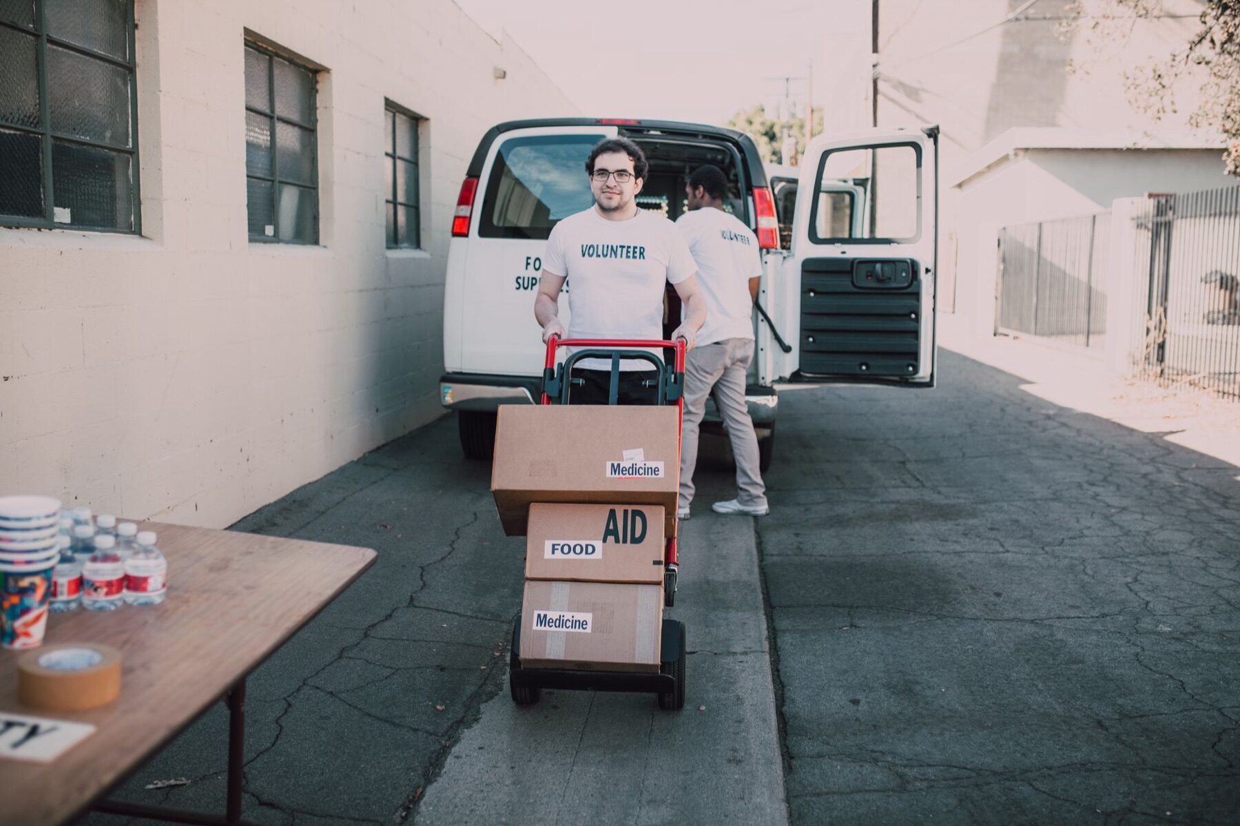 Volunteer wheeling a hand truck stacked with food aid boxes from a supply van